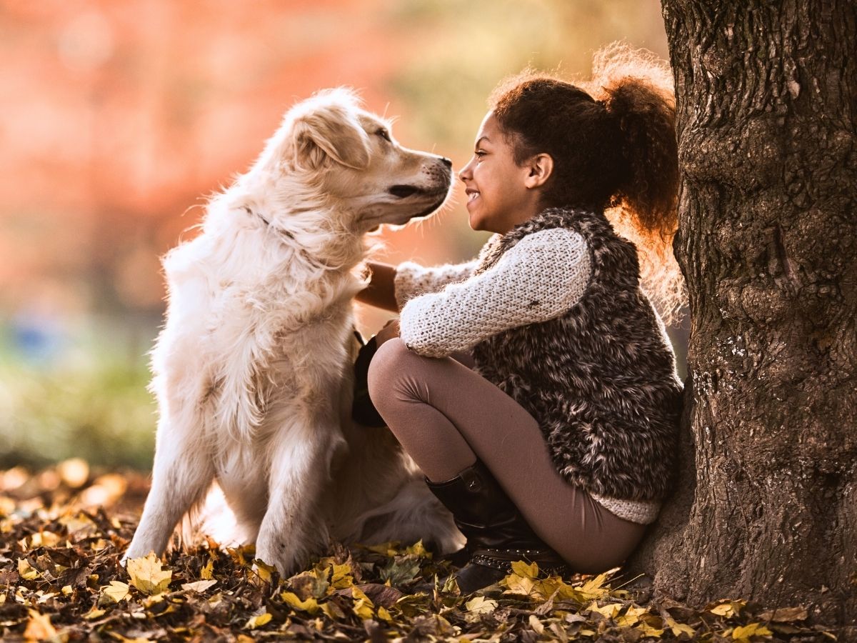 happy young girl hugging her golden retriever by a large tree